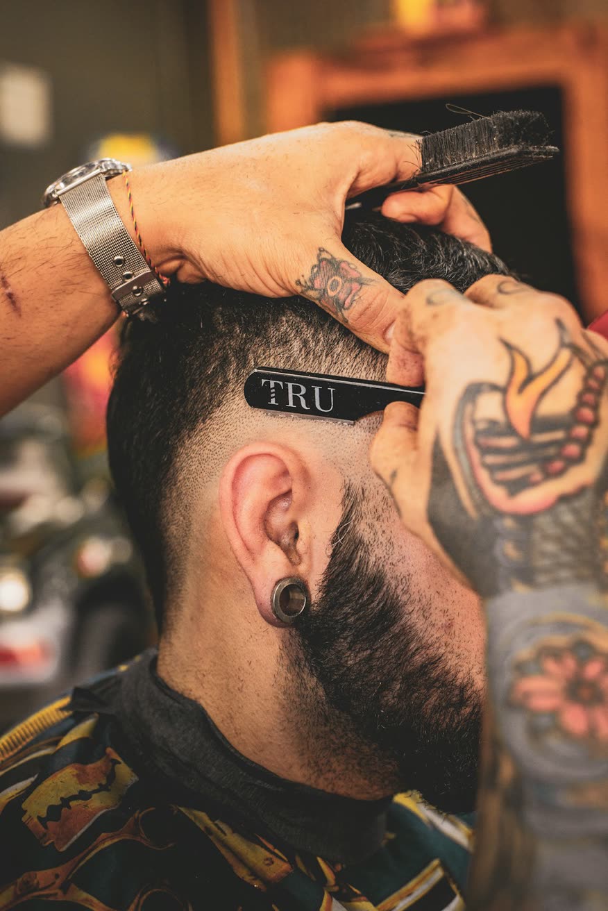 Barbeiro tatuado aparando o cabelo de um cliente com navalha