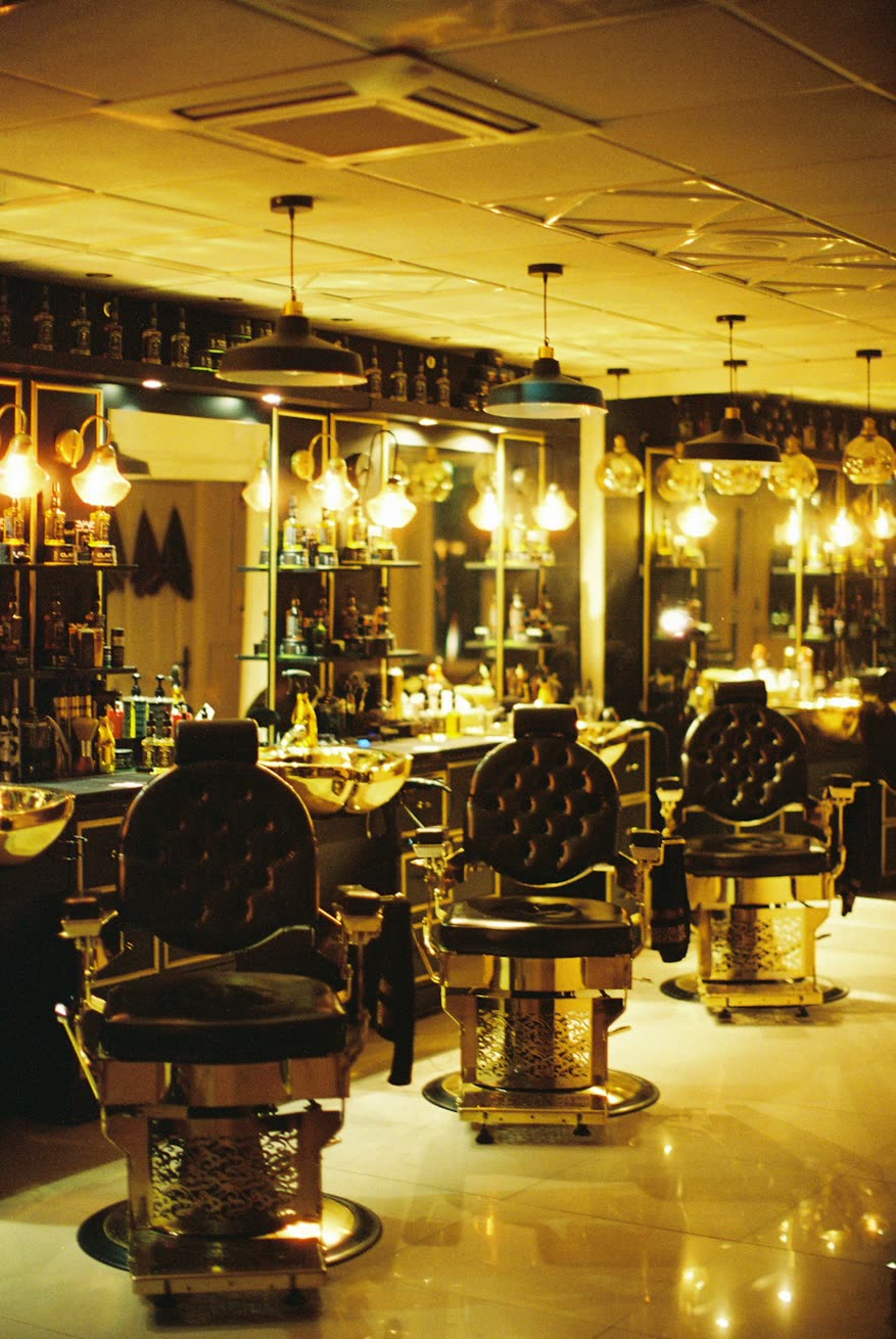 Salão de barbearia com cadeiras de couro e luz âmbar
