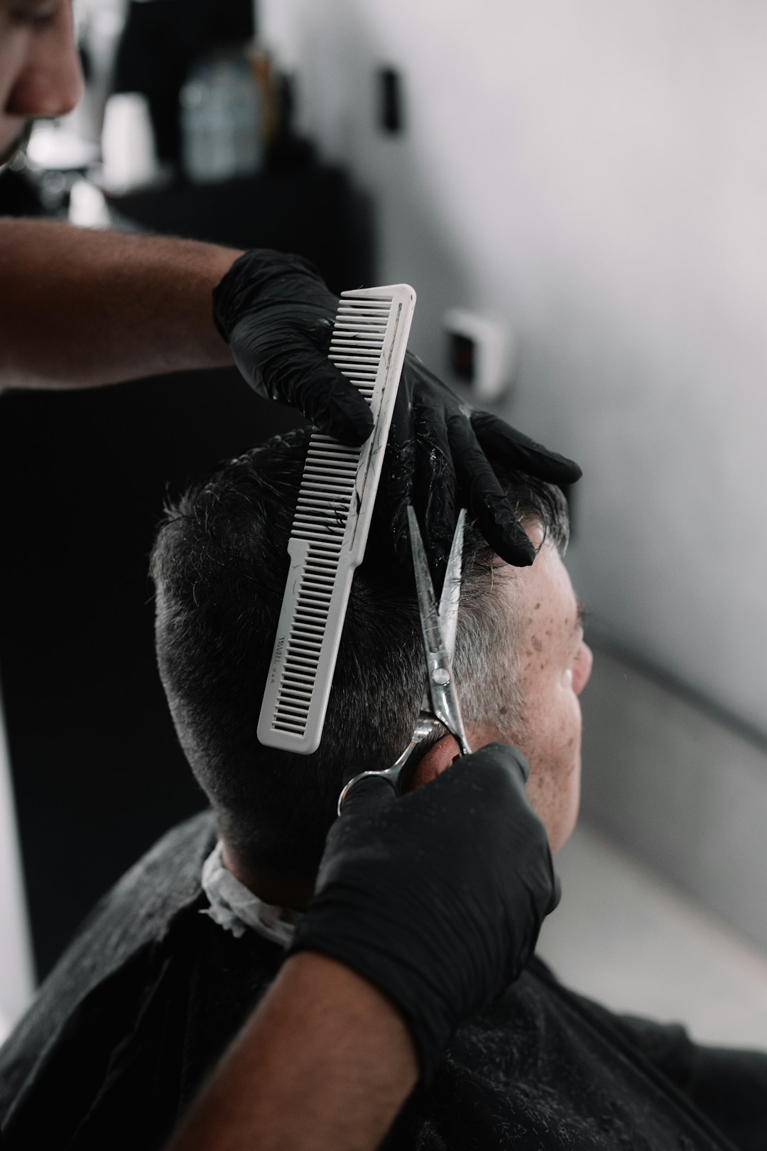 Barbeiro de luvas cortando cabelo com pente e tesoura